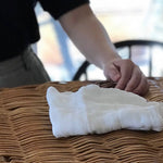 Lifestyle photo of Shirayuki Kitchen Cloth folded neatly on a woven basket, with hand reaching in—highlighting its natural texture and everyday beauty.”