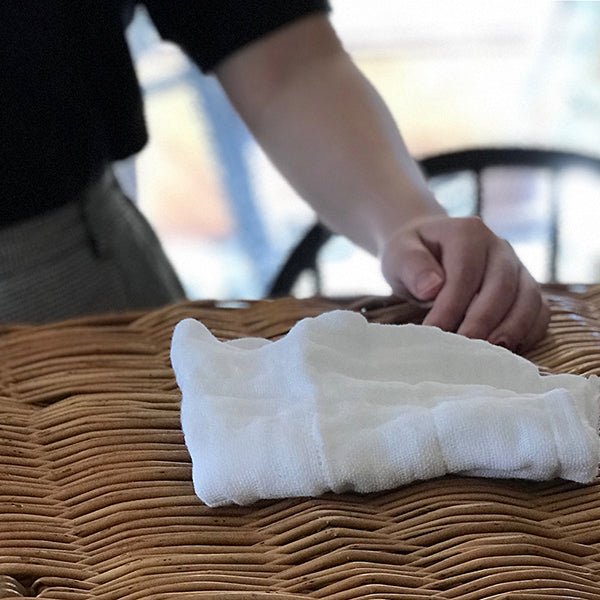 Lifestyle photo of Shirayuki Kitchen Cloth folded neatly on a woven basket, with hand reaching in—highlighting its natural texture and everyday beauty.”