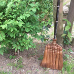 Shojiya Denbei Shuro Broom leaning against a tree in a Japanese garden, showcasing its natural materials and traditional craftsmanship.