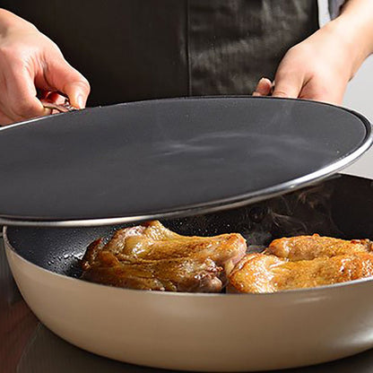 Person lifting a splatter screen off a frying pan with sizzling chicken thighs, showing how it controls oil splatter while cooking meat on the stovetop